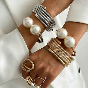Detail of layered gold and silver snake chain bracelets with large pearls on white suit