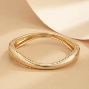 Close-up of polished gold-tone wavy bangle with asymmetrical design and hinge mechanism