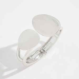 Close-up of a silver minimalist bangle featuring asymmetric oval plates and a hinged clasp
