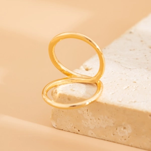 Detail shot of golden minimalist double-loop geometric ring on a textured stone base