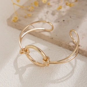 Detail of golden knot cuff bracelet with central ring on elegant marble background