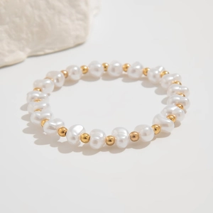 Detailed macro view of baroque pearl and gold bead elastic bracelet on textured stone