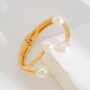 Detalle macro del brazalete chapado en oro con cuatro perlas blancas redondas