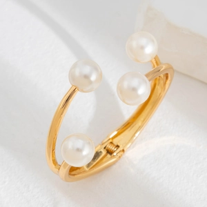 Detalle de brazalete abierto dorado de varias capas con elegantes perlas blancas sobre piedra