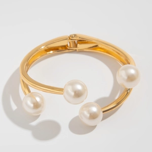 Detalle de brazalete dorado texturizado con perlas blancas y cierre de bisagra elástica