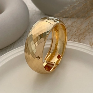 Detalle macro de pulsera dorada con superficie facetada y cierre de resorte metálico