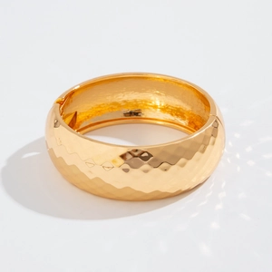 Detalle de brazalete ancho dorado martillado con textura geométrica y bisagra lateral
