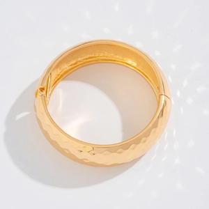 Vista detallada del brazalete rígido dorado con textura martillada y cierre de bisagra