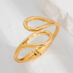 Detail of gold teardrop-shaped open spring bracelet with smooth metallic mirror finish