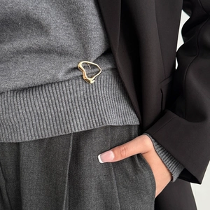 Detailed view of an irregular wavy gold brooch on a grey sweater with a modern abstract design