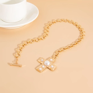 Detail van een gouden schakelketting met kruishanger met parels en een handige T-sluiting