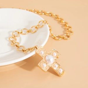 Close-up of golden chunky chain necklace with a pearl cross pendant on a ceramic dish