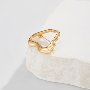 Macro shot of liquid metal gold brooch with irregular wavy texture on a white stone base