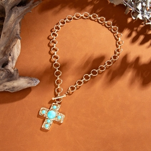 Close-up van gouden kruisketting met turquoise kralen en OT-sluiting op een warme ondergrond