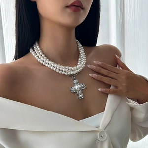 Detail of multi-layer pearl necklace with vintage silver cross pendant worn by model