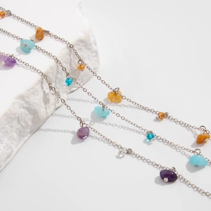 Delicate silver chain with colorful natural stones and pearls on white textured stone