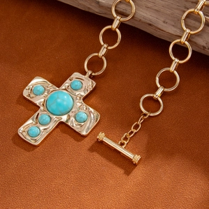 Close-up of golden cross pendant with turquoise stones on thick metal chain