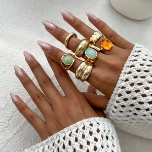 Close-up of golden alloy ring set with green and orange gems on a hand model