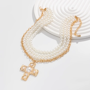 Detail of multi-layer pearl necklace with a vintage gold cross pendant on a white tray
