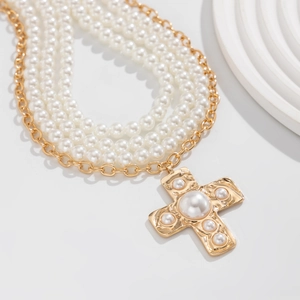 Macro detail of layered pearl necklace with gold chain and cross pendant featuring pearls