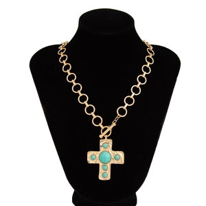 Detail van gouden ketting met kruishanger en turquoise inlays op een zwarte buste display