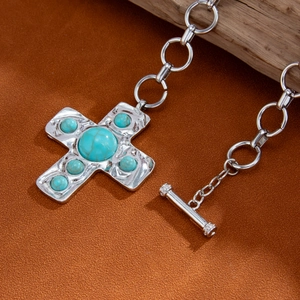 Retro kruis hanger ketting met turkoois stenen en toggle sluiting op een suède achtergrond