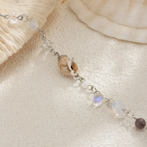 Détail de breloque coquillage et perles sur une chaîne délicate sur fond de sable blanc
