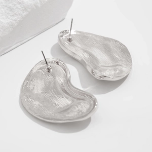 Macro detail of silver irregular drop earrings showing brushed metal texture and back pin