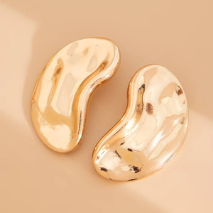 Macro detail of golden teardrop earrings with irregular hammered texture and metallic shine