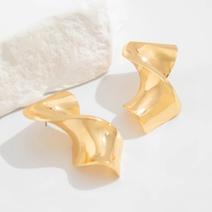 Macro view of gold twisted teardrop earrings on white rock showing polished texture