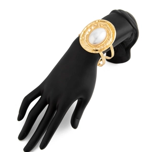 Dettaglio del bracciale rigido dorato in metallo liquido con perla ovale e texture martellata