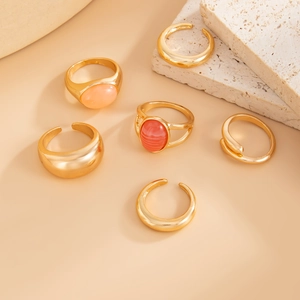 Close-up of a 6-piece set of gold rings with acrylic gemstones on textured stone pedestals