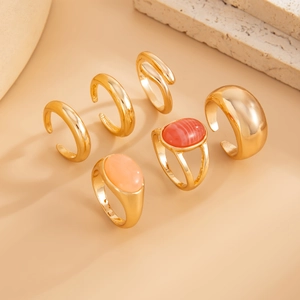 Close-up of a 6-piece golden ring set featuring pink and amber resin stones on stone plate
