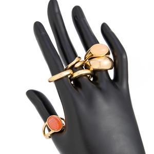 Close-up of gold metal ring set with oval orange and pink gemstones on black hand model