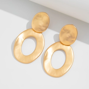 Detail of matte gold teardrop earrings with textured wave pattern on a white background