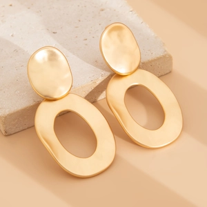 Macro detail of matte gold geometric oval earrings with irregular hammered texture