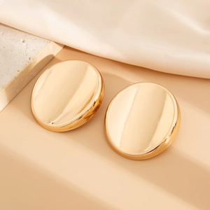 Macro shot of large polished golden oval stud earrings on an elegant satin backdrop