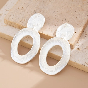 Macro shot of silver metal teardrop earrings with radial texture on beige stone