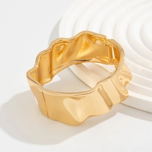 Detail view of gold wide cuff bracelet with wavy liquid metal texture and polished finish