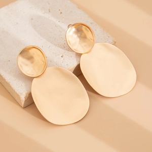Detail of gold metal drop earrings with brushed texture on organic stone background
