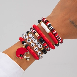 Detail of stacked rugby-themed bracelets with red heishi beads and gold helmet charm