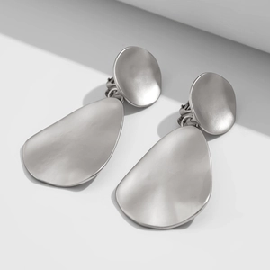 Detail of matte silver irregular teardrop earrings with brushed texture in modern style