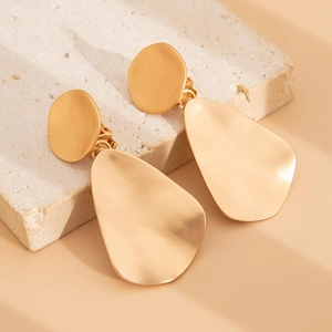 Detail of matte gold irregular teardrop earrings on a white stone tray texture