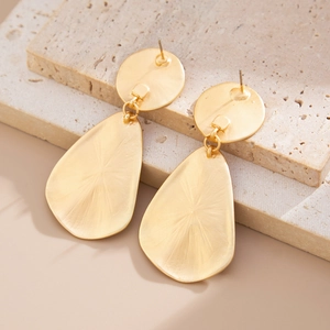 Close-up of matte gold geometric drop earrings on beige travertine decorative stones