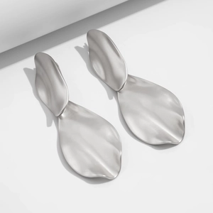 Macro detail of large matte silver leaf earrings with organic wavy edges and geometric shadows