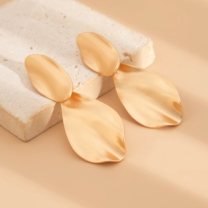 Detail of matte gold irregular water drop earrings on textured stone background