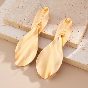 Macro shot of matte gold irregular wave leaf earrings with brand engraving detail