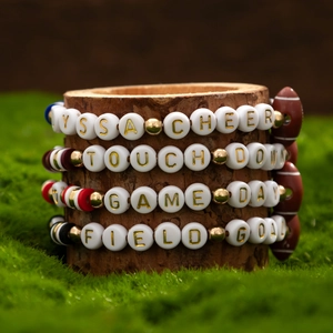 Detail of football-themed beaded bracelets with Cheer and Game Day lettering on a wood stand