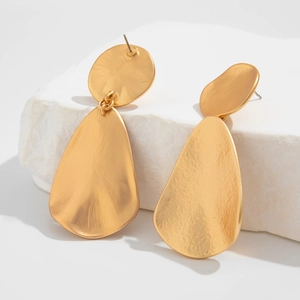 Macro view of gold folded teardrop earrings with hammered texture on white stone