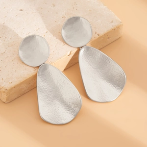Macro shot of silver geometric earrings with a hammered texture on textured stone